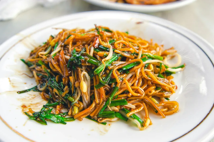 A plate of stir fried noodles with greens