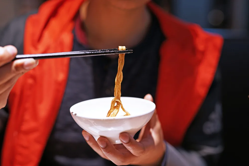 Chopsticks lifting noodles from a bowl