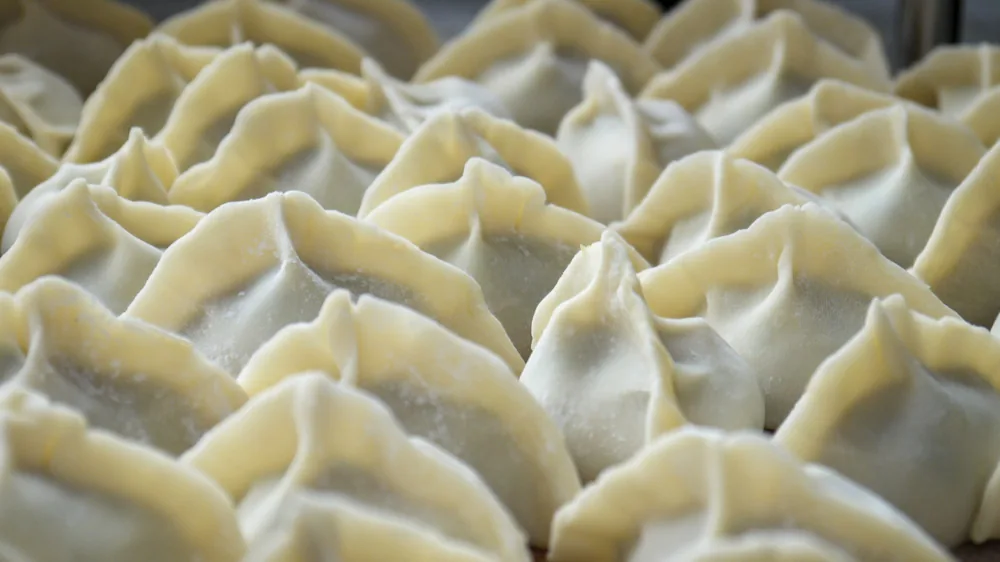 Pleated dumplings arranged on a tray before cooking