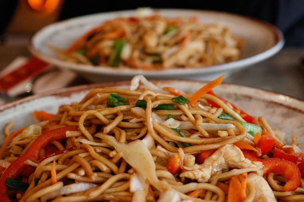 Noodles being tossed with tongs in a wok