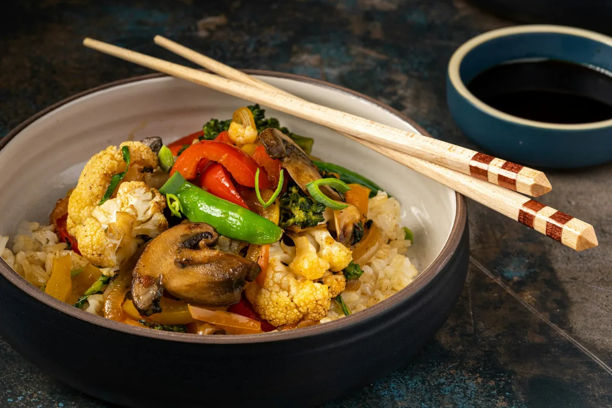 A bowl of stir fried meat and vegetables with chopsticks