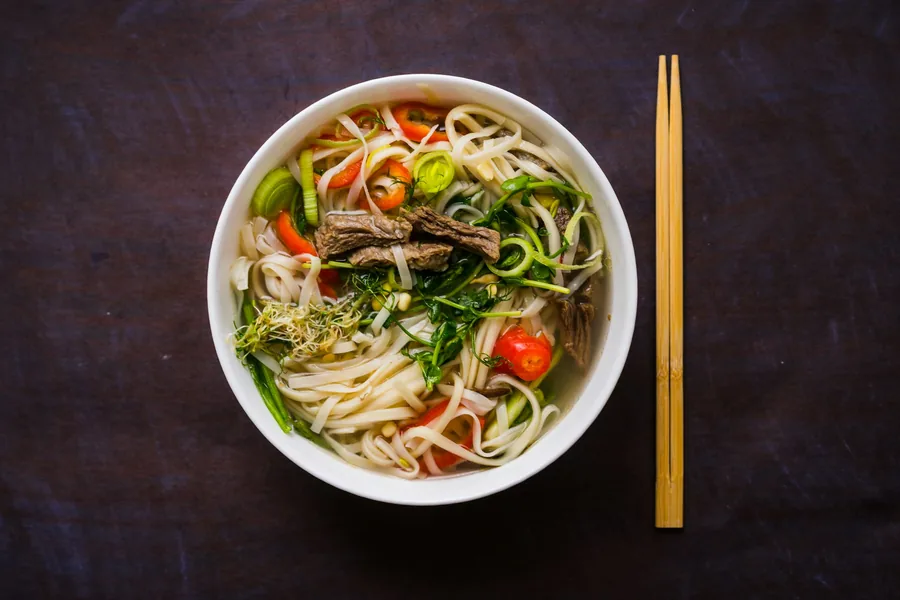Bowl of lo mein noodles with vegetables and chopsticks